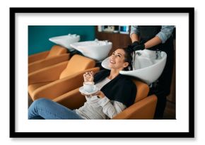 Happy woman enjoys in cup of coffee during hair wash at hairdresser's.