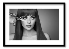 Beautiful young woman with a bright makeup and a smooth long hair holds metal scissors. Hair salon, haircut. Care and beauty hair products. Perfect make-up