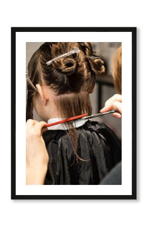 Rear view of hand of hairdresser doing haircut of child with hair clips on her hair in hair salon. Hairtician. Back view. Hairdressing Services. Modern Children Haircut