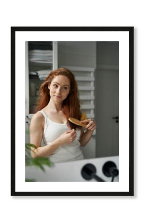 Young caucasian woman brushing hair in the bathroom