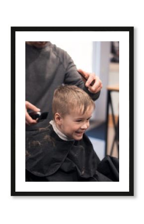 Toddler boy happy to be on the haircut with a professional children's hairdresser. little boy having a haircut at hair salon. Hairdresser's hands making hairstyle to child