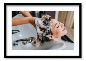 Professional hairdresser washing hair of a beautiful young  woman in hair salon.