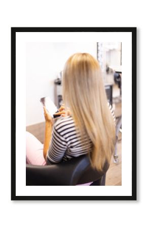 Blonde woman with long hair and with a phone in her hands at hairdressing salon.