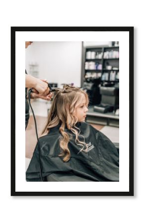 hands of a hairdresser with a curling iron make a hairstyle to a curly girl in a professional beauty salon