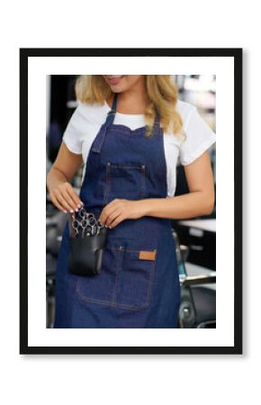 Cropped image of smiling young hairdresser taking scissors out of tool belt