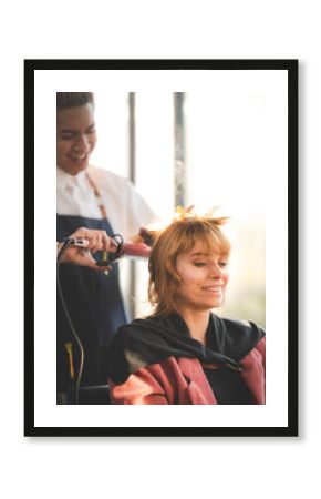 Smiling young woman curling hair with machine by male stylist in modern salon for a hairdo and new fashion trend