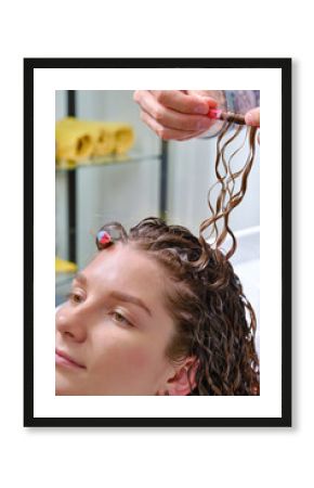 Woman with wavy curls. Woman with brown curly hair in a beauty salon. Creating hairstyles by a hairdresser in the salon. Hands hairdresser doing a perm rolling the hair. Shallow depth of field.