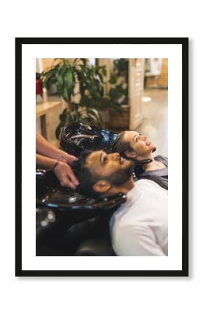 Indian male client having his hair washed by hairdresser next to blonde female customer in a professional hair salon. High quality photo 