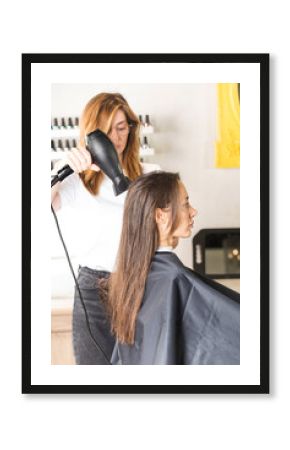 The hairdresser dries the client's hair with a hair dryer and styles her hair with a comb.