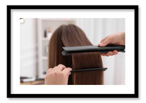 Hairdresser straightening woman's hair with flat iron in salon, closeup