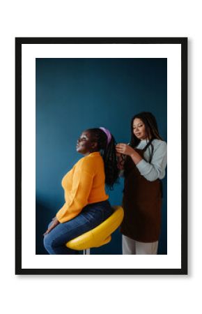 Confident African hairdresser braiding hair to a female customer on blue background