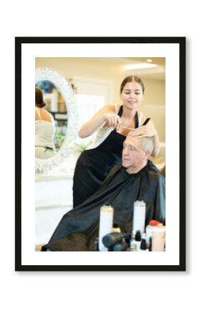 Young girl, professional hairstylist making haircut to elderly male client in hairdressing salon, skillfully using scissors..