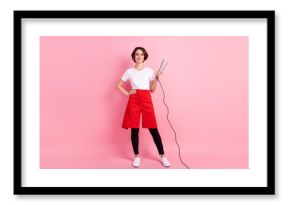 Full length body size photo of hairdresser keeping hot hair straightener smiling isolated on pastel pink background