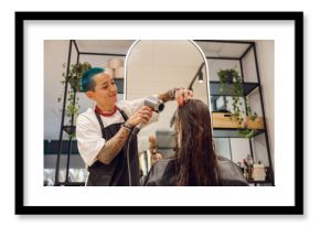 Smiling female hairdresser dries hair of client with a hairdryer in beauty salon