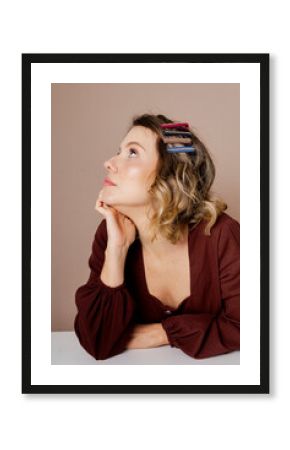 Bored young woman with dark blond hair and brown blouse on isolated beige background. Using hair accessories.