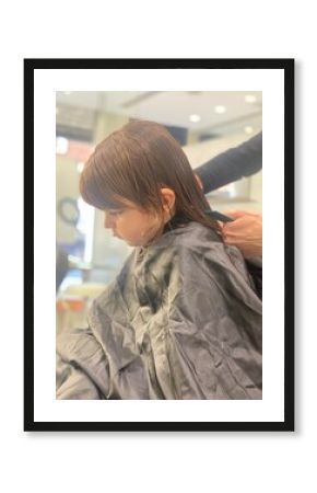  Side view of a young boy receiving a haircut from a stylist in a salon, covered with a cape.