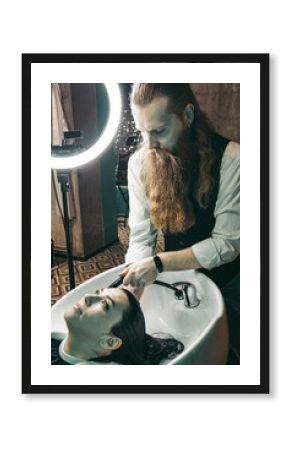 Hairdresser washing woman's hair. Man young hairdresser professional experienced in vest with long beard and hair ,washing hair head female client in hairdressing salon .medium shot 