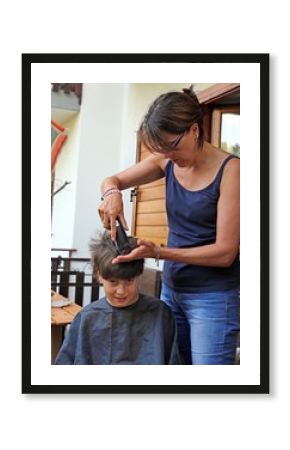 Young mom cuts the hair of her son with the razor at home