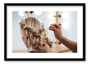 Female hairdresser making hairstyle to blonde girl in beauty salon.