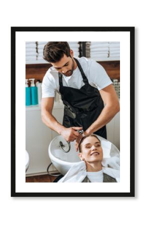 handsome young hairdresser washing hair to smiling young woman in beauty salon