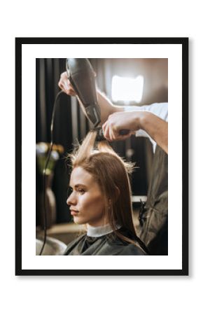 Cropped shot of hairstylist drying hair to beautiful young woman in beauty salon