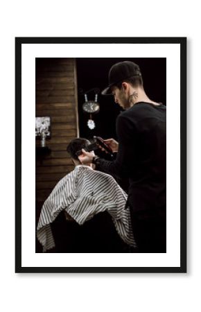 The fashion  barber makes a razor cut hair for a stylish black-haired man in a stylish  barbershop