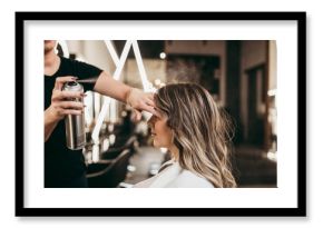 Beautiful young woman with long curly hair in hair salon. Professional hairdresser styling with hairspray.
