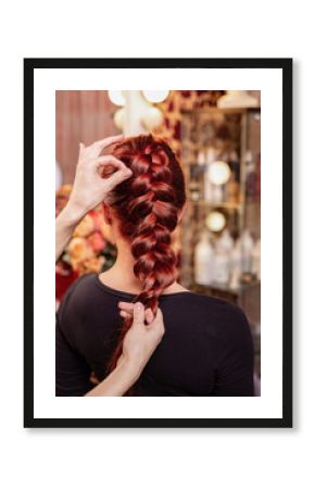 Beautiful, red-haired girl with long hair, hairdresser weaves a French braid, in a beauty salon. Professional hair care and creating hairstyles.