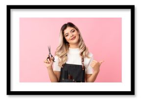 Teenager girl over isolated pink background with hairdresser or barber dress and pointing it