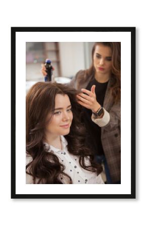 Hairdresser using hairspray while styling hair of a lovely young woman