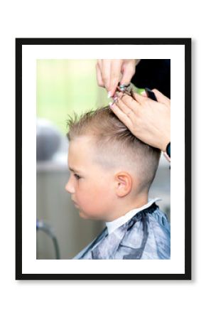 Serious school boy ready getting trendy haircut from expirienced barber at fashionable hairdressing salon.