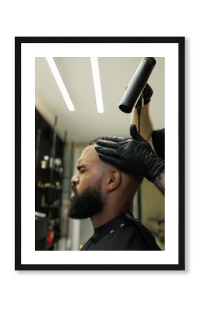 Barber drying hair of young african american man in barbershop