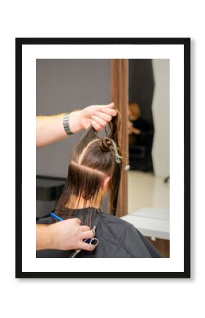 Male hairdresser holds and splits long hair of a young brunette woman in a hair salon