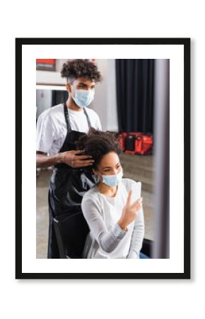 African american hairdresser touching hair of client with smartphone