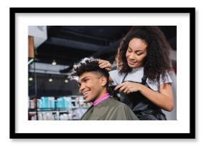 Smiling african american hairdresser in apron trimming neck of client in salon