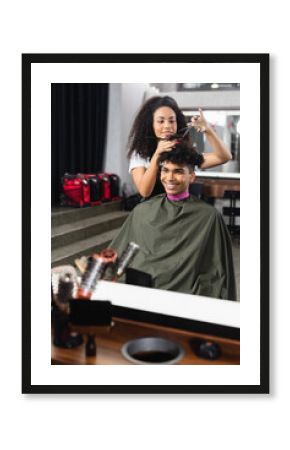 African american hairdresser holding scissors and comb near hair of cheerful man