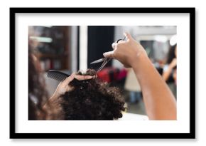 Cropped view of african american hairdresser on blurred foreground holding comb and cutting hair of man