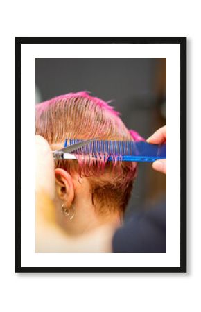 Young caucasian woman with pink hair getting a short haircut by a male hairdresser's hands in a hairdressing salon