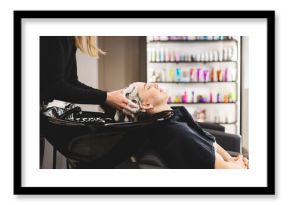 Master woman hairdresser washes hair of a girl with shampoo before styling in a beauty salon.