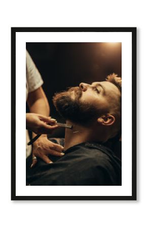 Man getting shaved with straight edge razor by hairdresser at barbershop