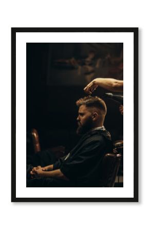 Young bearded man getting haircut by hairdresser