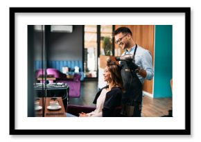 Young happy woman getting her hair styled by male hairdresser at the salon.