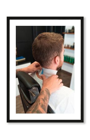 Hairdresser with tattoos putting a neck strip around the customer's neck under the lights