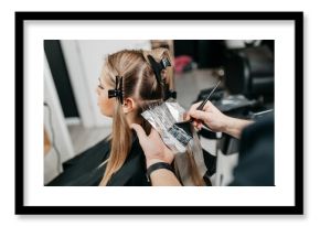 Hairdresser is applying bleaching powder on woman's hair and wrapping into the foil.