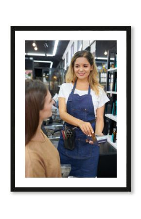 Smiling hairdresser swiping credit card when accepting payment from female client