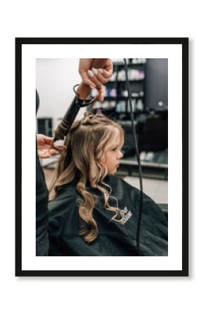 Female hands of a hairdresser. Close-up of blond hair on a curling iron. Curling curls. Beauty saloon.