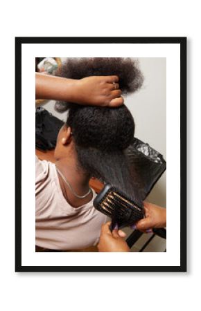 femme noire africaine aux cheveux frisés et longs faisant un lissage chez une coiffeuse ave cun ebrosse chauffante 