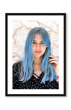 Portrait of a beautiful blue-eyed woman with blue hair looking into the camera against a light marble wall. Hair dyeing, coloring. Hair care, hairdressing, trichology