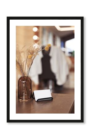 Barber business cards near glass vase with dried flowers on wooden table in hairdressing salon. Space for text