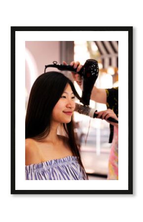 hair stylist combing with brush and dryer the straight hair of a young asian woman in the hairdressing salon, beauty care and wellness concept